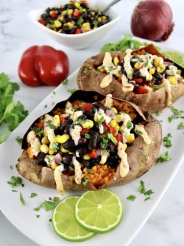 vegan black bean stuffed sweet potatoes with chipotle drizzle on top and lime slices on side