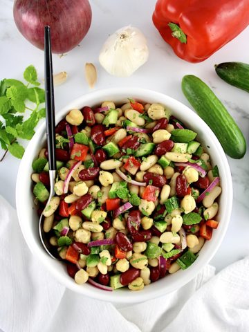 Easy Bean Salad in white bowl with spoon and fresh veggies in background