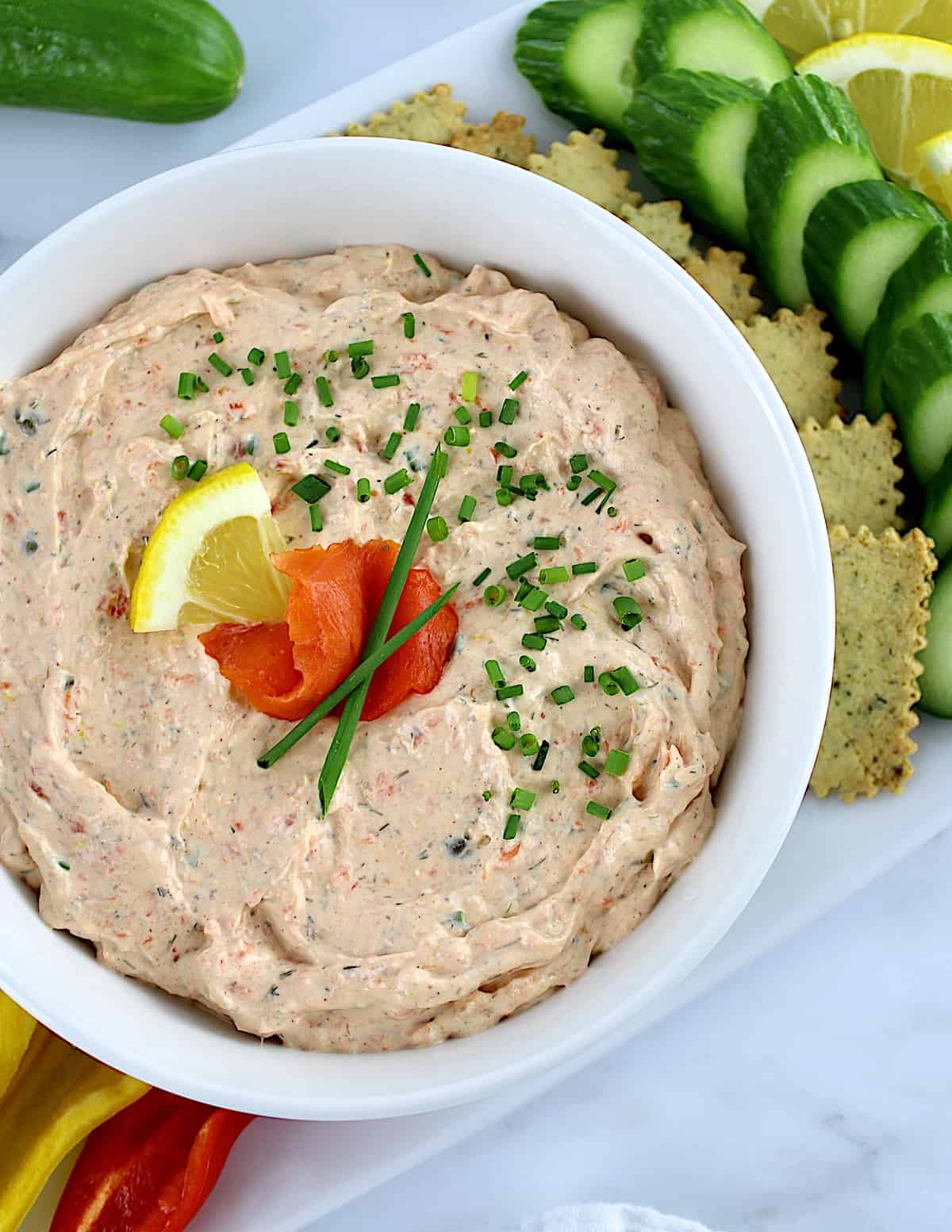 Smoked Salmon Dip in white bowl with mini peppers, crackers and cucumber slices on side