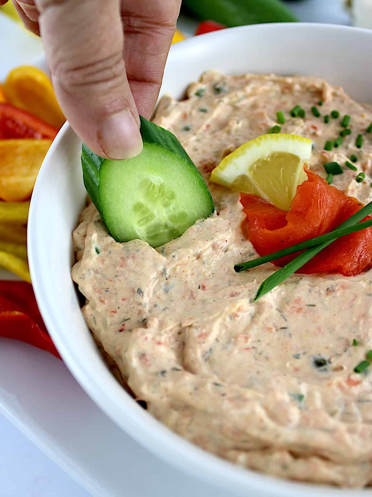 dipping cucumber slice into Smoked Salmon Dip in white bowl