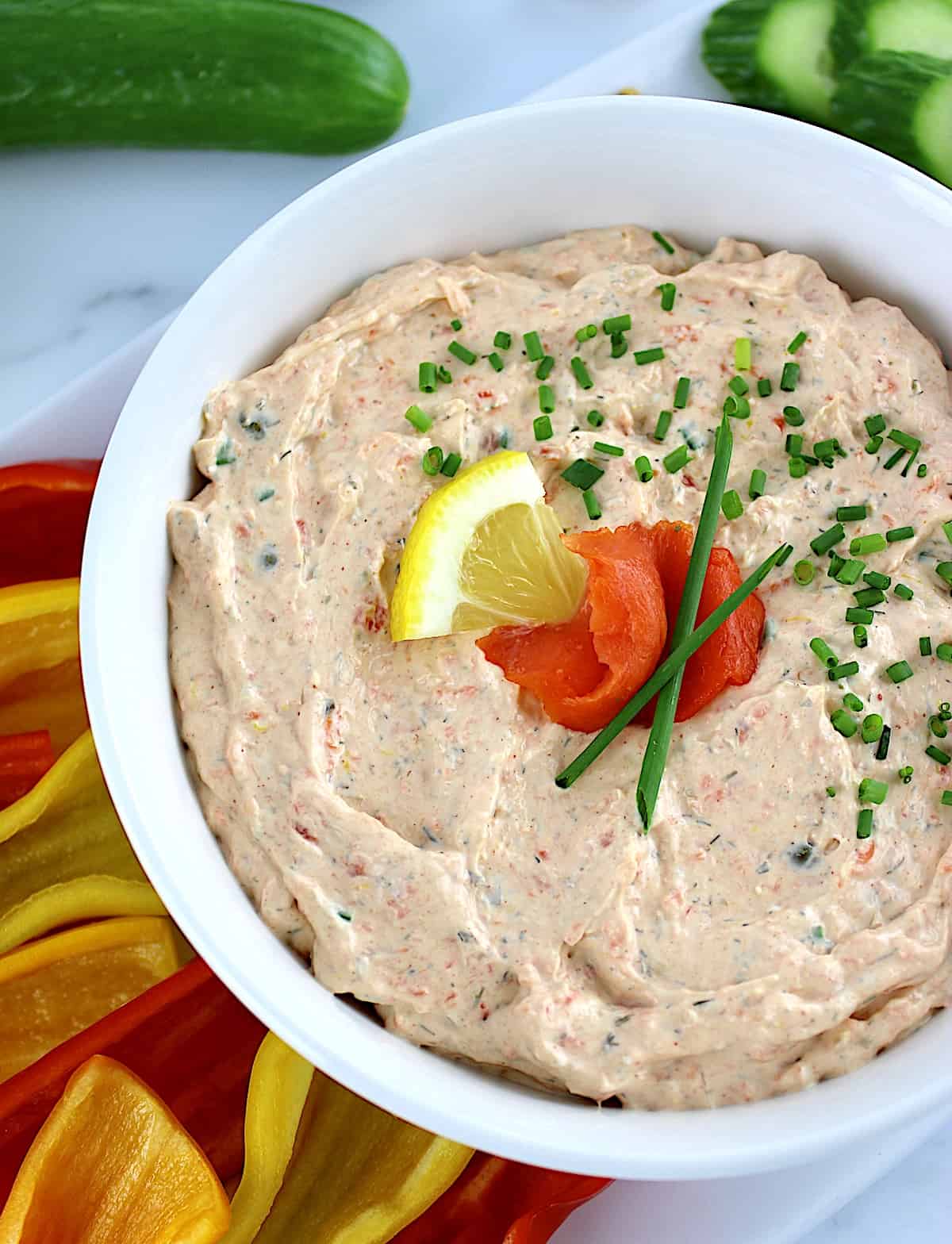 Smoked Salmon Dip in white bowl with mini peppers, crackers and cucumber slices on side