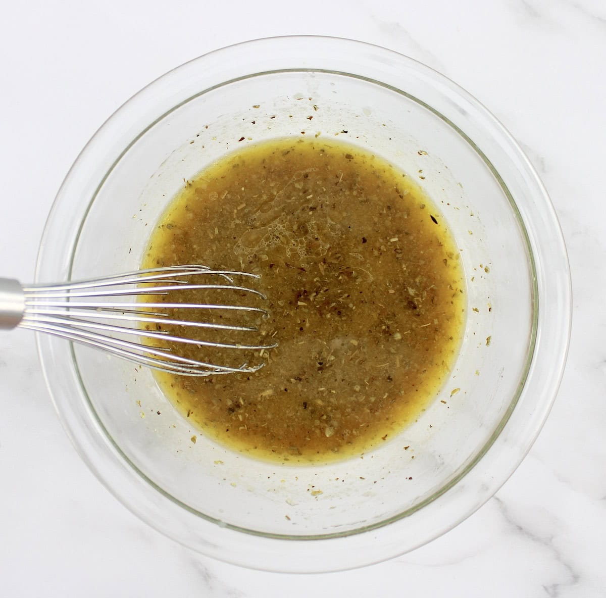 Greek chicken kebab marinade ingredients in glass bowl with whisk