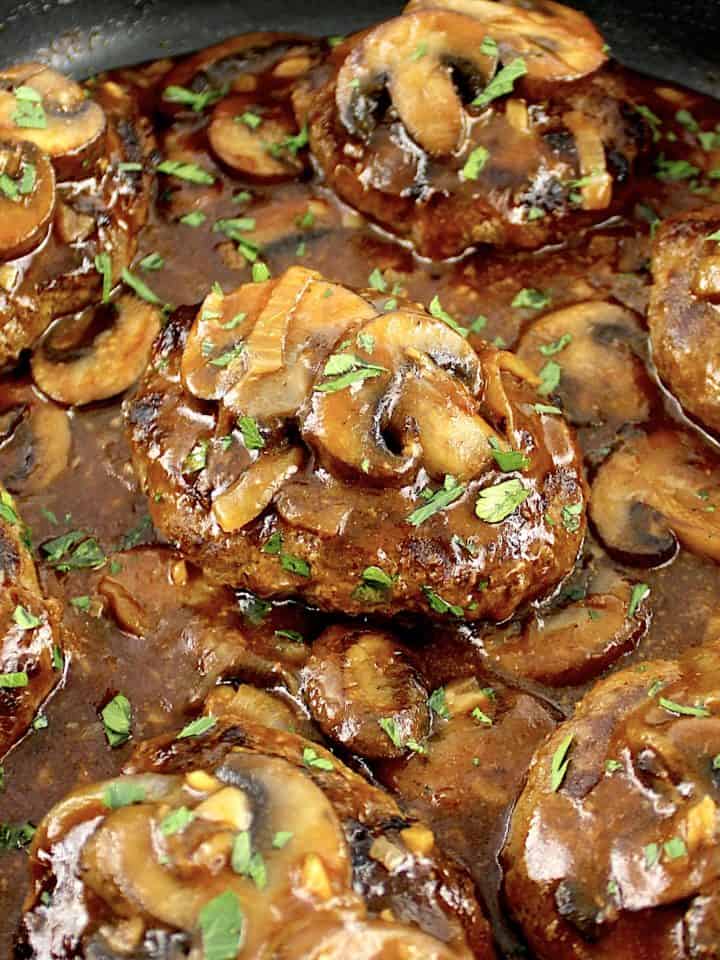 closeup of Salisbury Steak in skillet with gravy and mushrooms on top