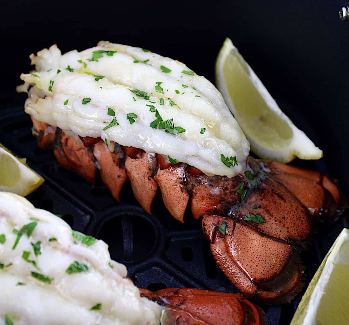 2 Air Fryer Lobster Tails in air fryer basket with lemon wedges