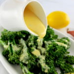 Beurre Blanc Sauce being poured out over broccoli on white plate with lemon in back