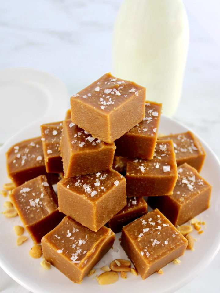 Peanut Butter Fudge slices stacked up on white plate with glass milk bottle in back