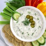 Dill Pickle Dip in white bowl with raw veggies and crackers around
