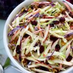 Apple Cranberry Slaw in white bowl with cabbage in back
