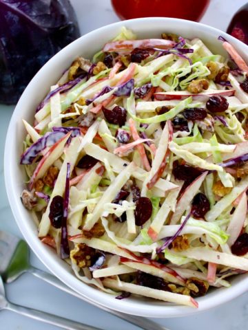 Apple Cranberry Slaw in white bowl with cabbage in back