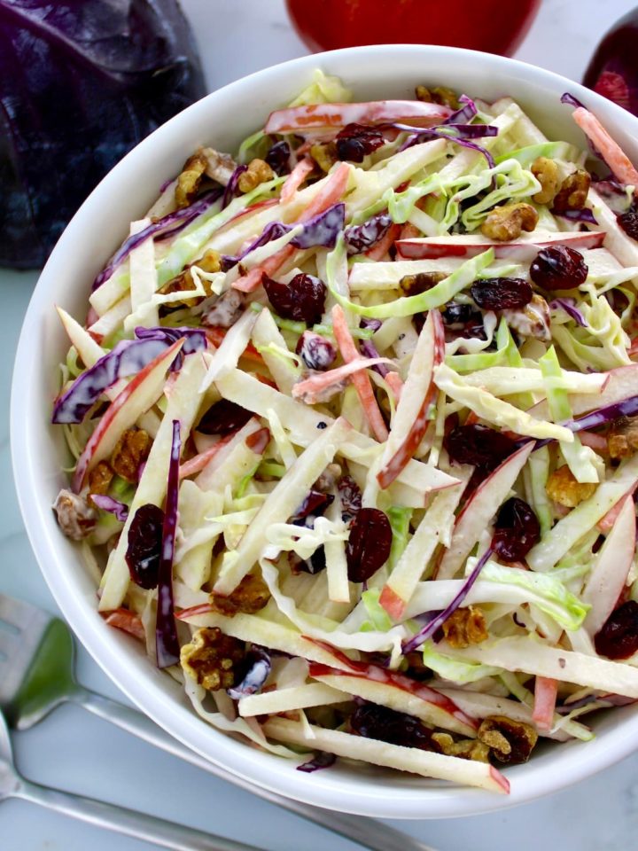 Apple Cranberry Slaw in white bowl with cabbage in back