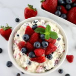 Berry Cheesecake Salad in white bowl with fresh berries and mint on top with berries in background