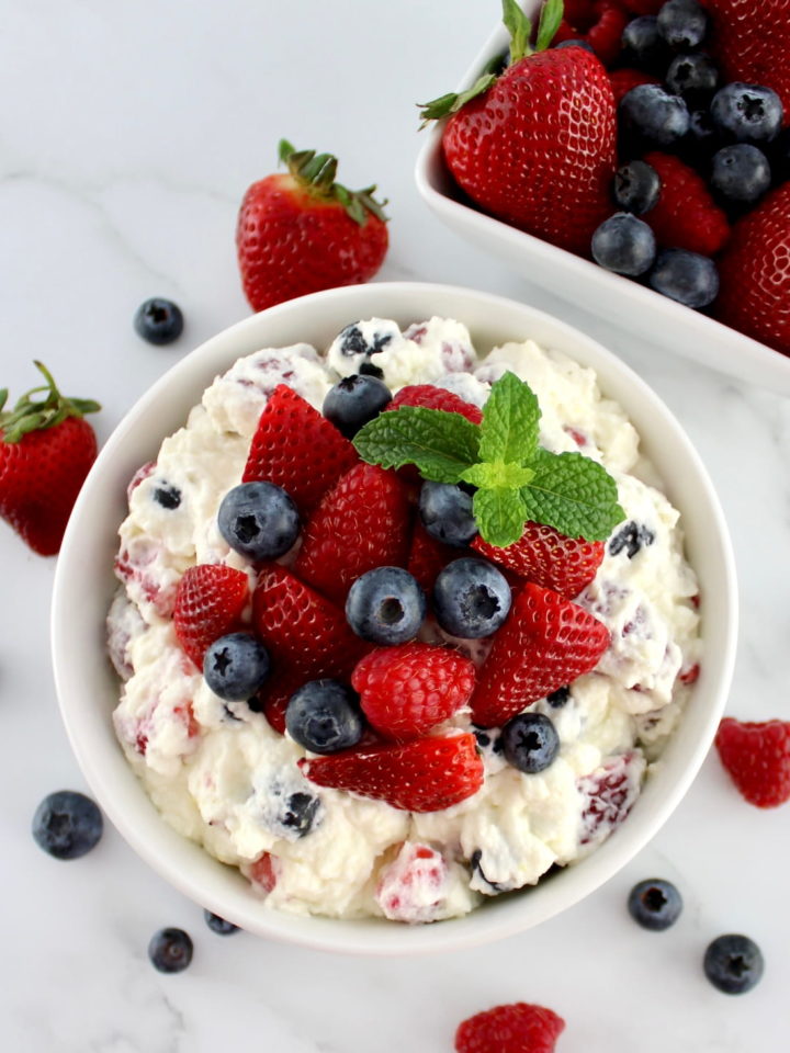 Berry Cheesecake Salad in white bowl with fresh berries and mint on top with berries in background