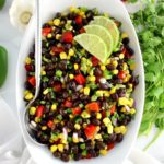 Black Bean Salad in white bowl with 3 lime slices and serving spoon