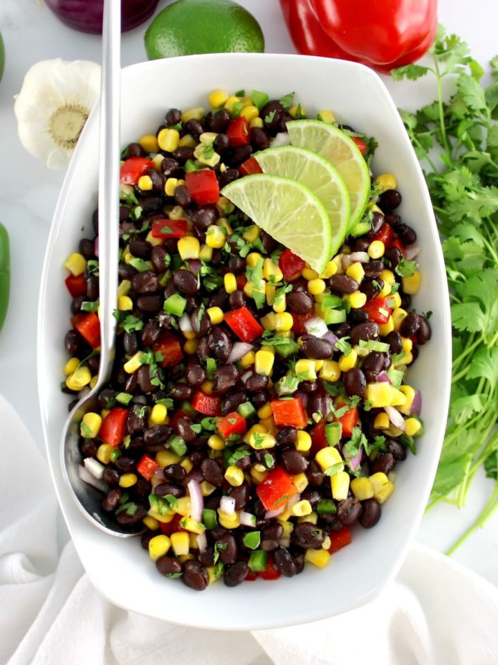 Black Bean Salad in white bowl with 3 lime slices and serving spoon