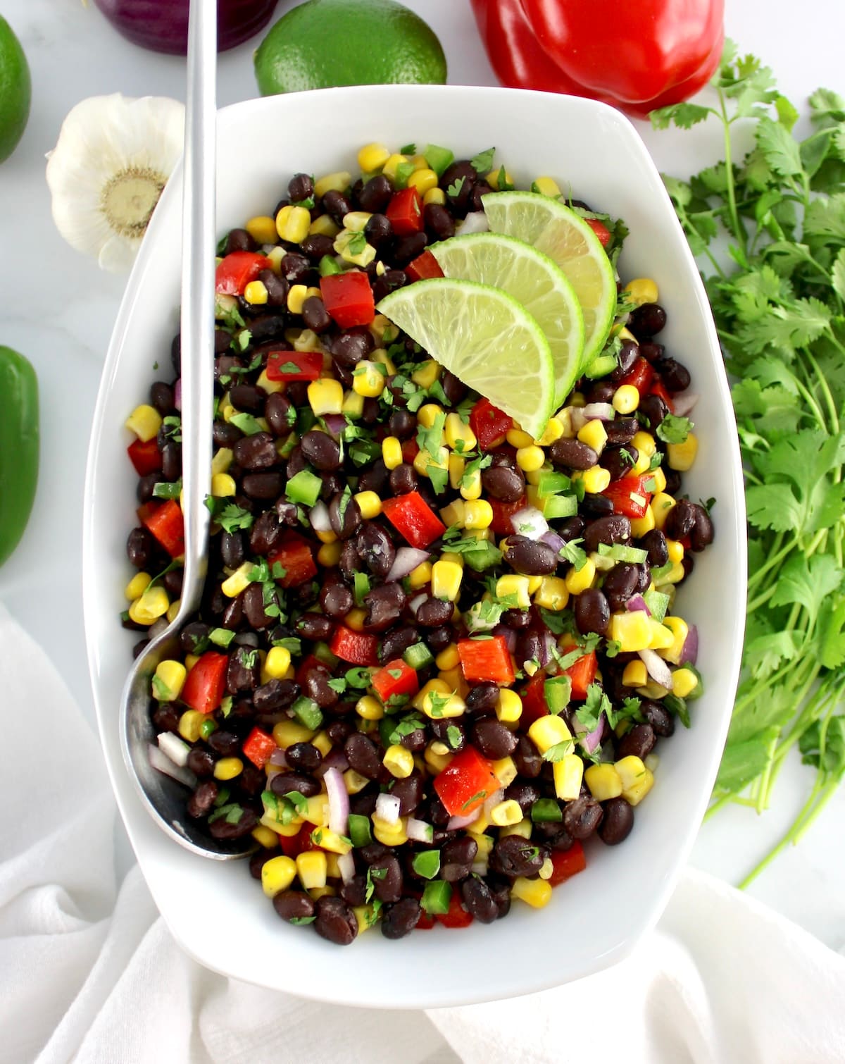 Black Bean Salad in white bowl with 3 lime slices and serving spoon