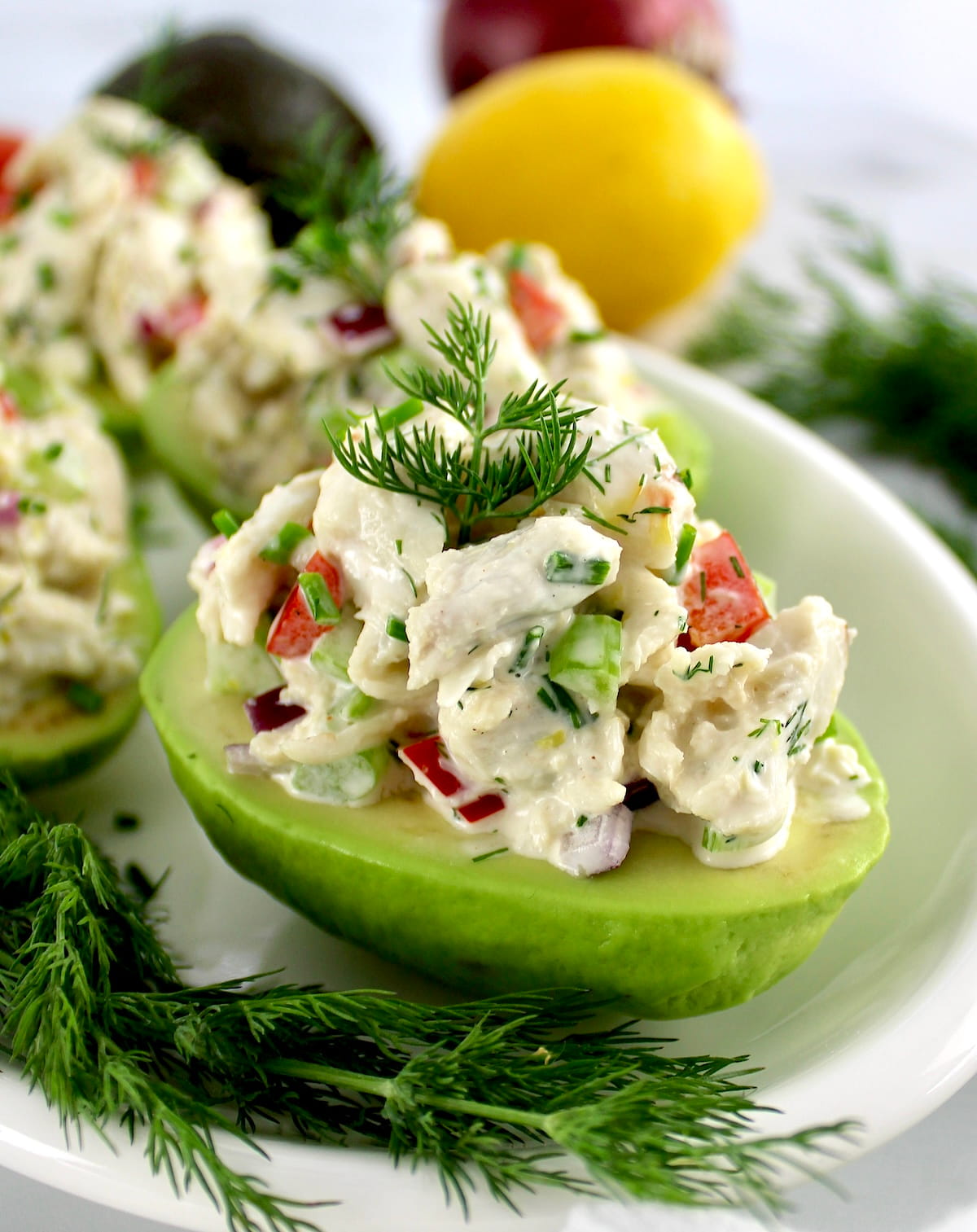 closeup of Crab Salad Stuffed Avocado on white plate with lemon and fresh dill in back