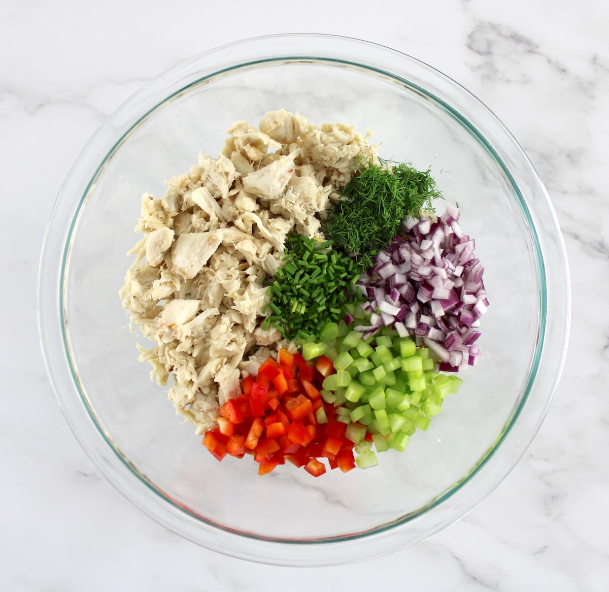 crab meat, herbs, red onion, celery and red bell pepper all chopped in glass bowl in sections