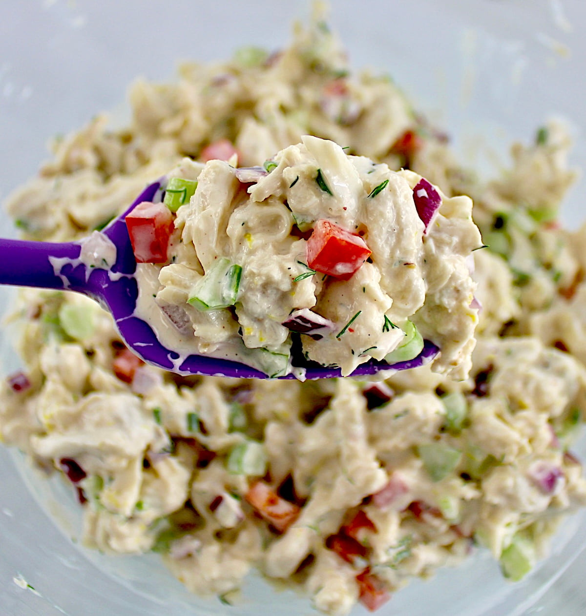 crab salad in glass bowl with purple spoon holding up some