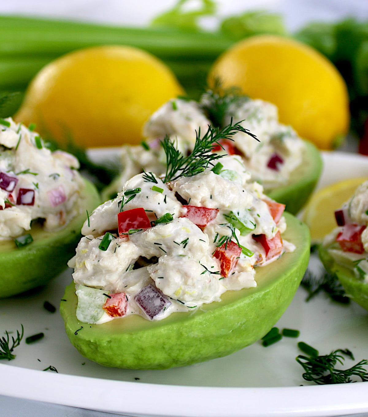 closeup of Crab Salad Stuffed Avocados on white plate with lemons in back