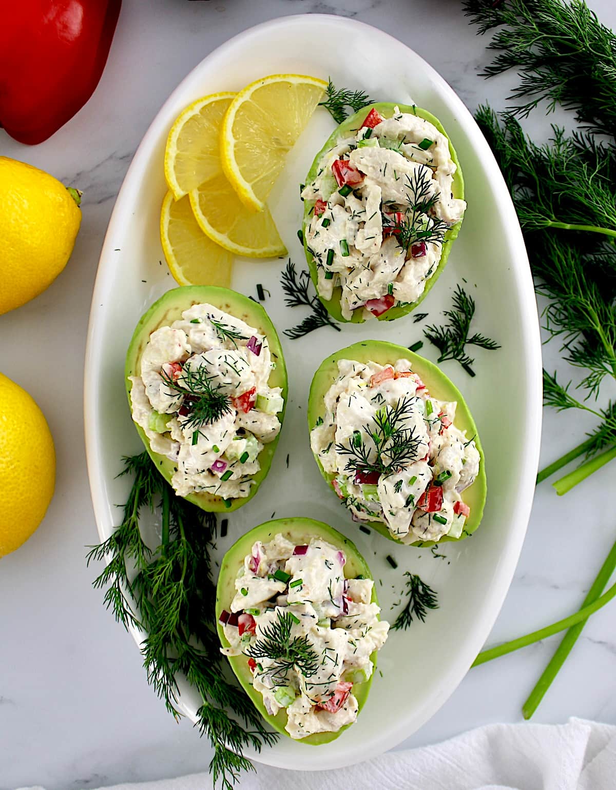 overhead view of Crab Salad Stuffed Avocados on white plate with lemon and fresh dill on side