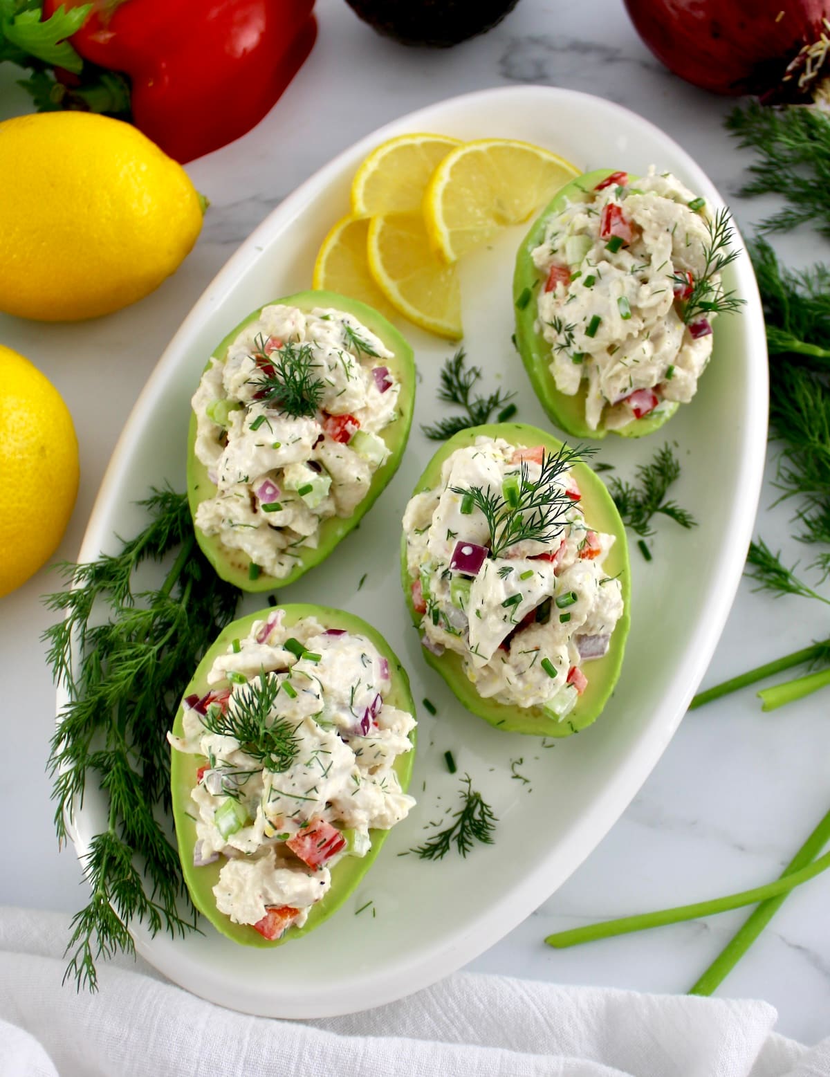 overhead view of Crab Salad Stuffed Avocados on white plate with lemon and fresh dill on side