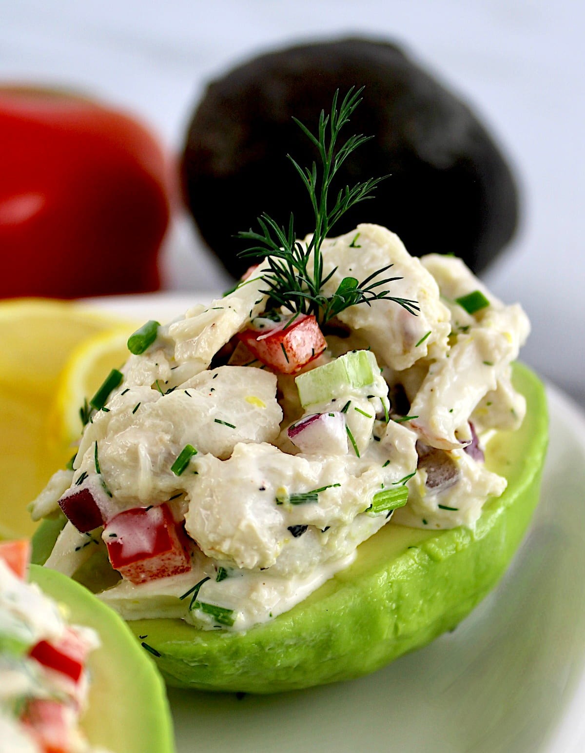 closeup of Crab Salad Stuffed Avocados on white plate with avocado and pepper in back