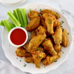 overhead view of Crispy Oven Baked Chicken Wings on white plate with buffalo sauce and celery sticks