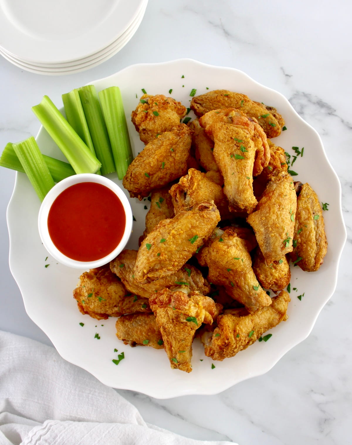 overhead view of Crispy Oven Baked Chicken Wings on white plate with buffalo sauce and celery sticks