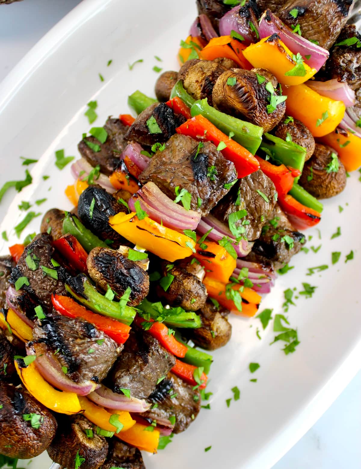 Grilled Beef Kebabs on white plate with chopped parsley