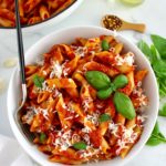 Penne Arrabbiata in white bowl with fork and white skillet in back
