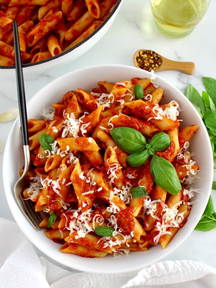 Penne Arrabbiata in white bowl with fork and white skillet in back