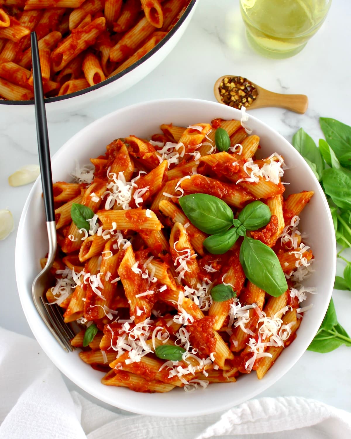 Penne Arrabbiata in white bowl with fork and white skillet in back