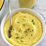 Creamy Parmesan Polenta in white bowl with spoon and fresh thyme on top