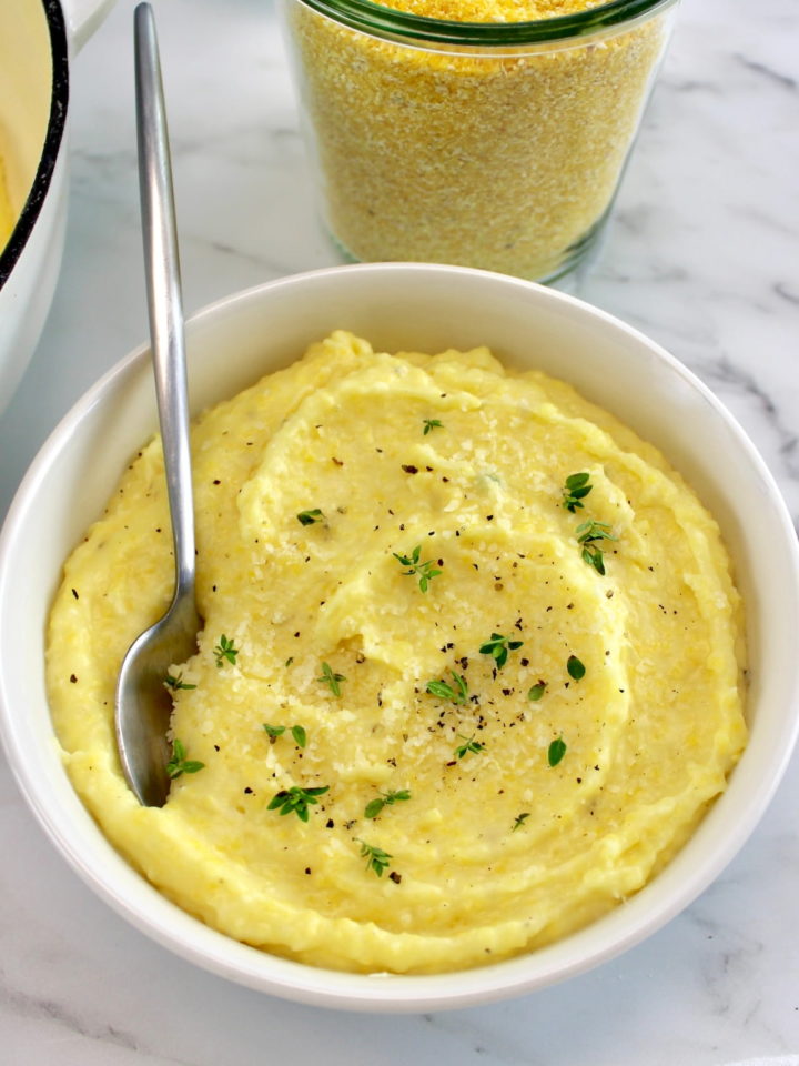 Creamy Parmesan Polenta in white bowl with spoon and fresh thyme on top