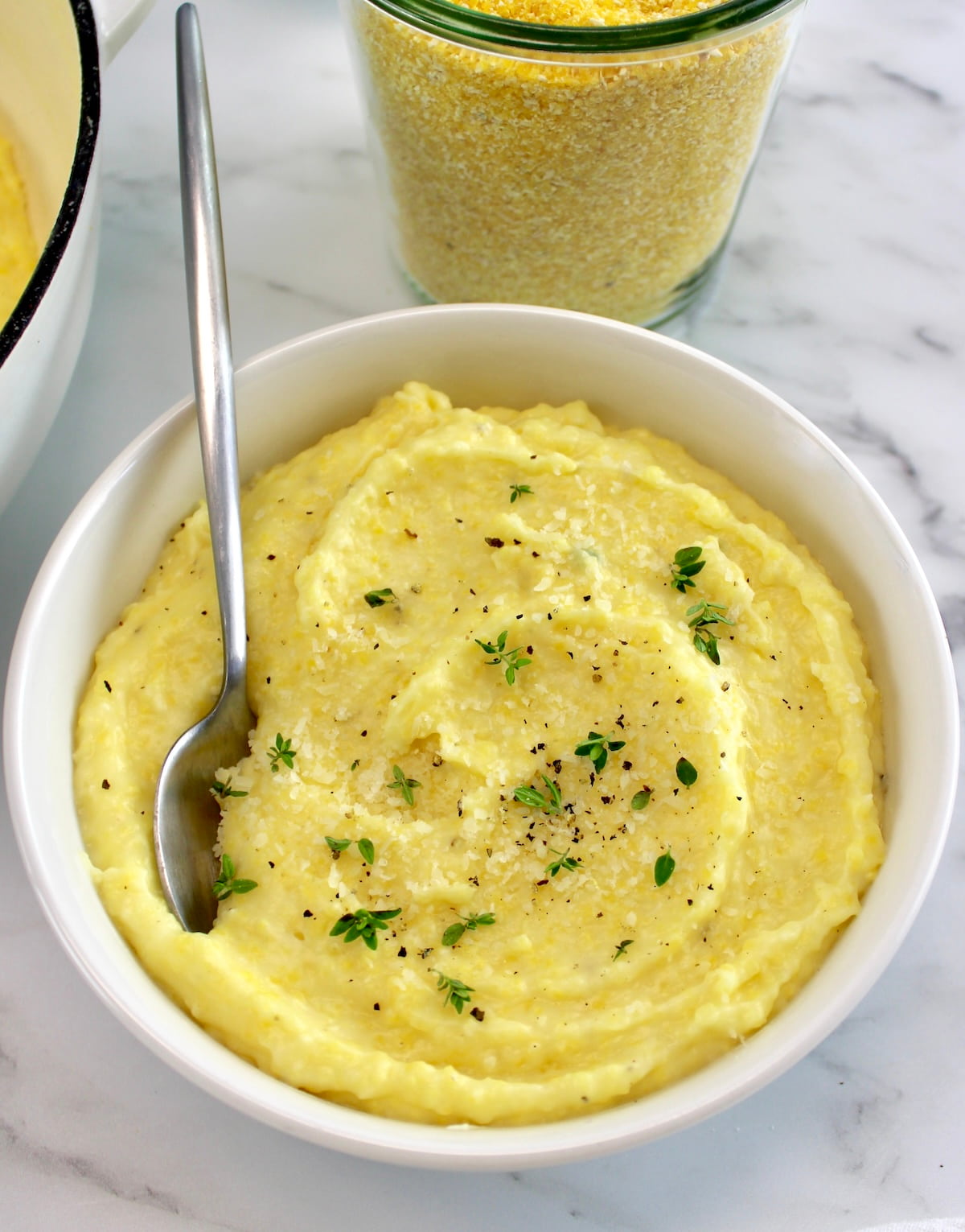 Creamy Parmesan Polenta in white bowl with spoon and fresh thyme on top