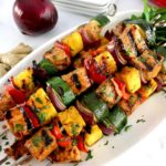 Grilled Hawaiian Pork Kebabs on white plate with chopped parsley and red onion in back