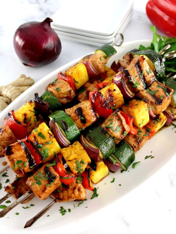 Grilled Hawaiian Pork Kebabs on white plate with chopped parsley and red onion in back