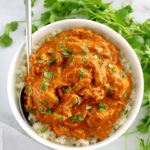 Slow Cooker Butter Chicken in white bowl over cauliflower rice with spoon on side