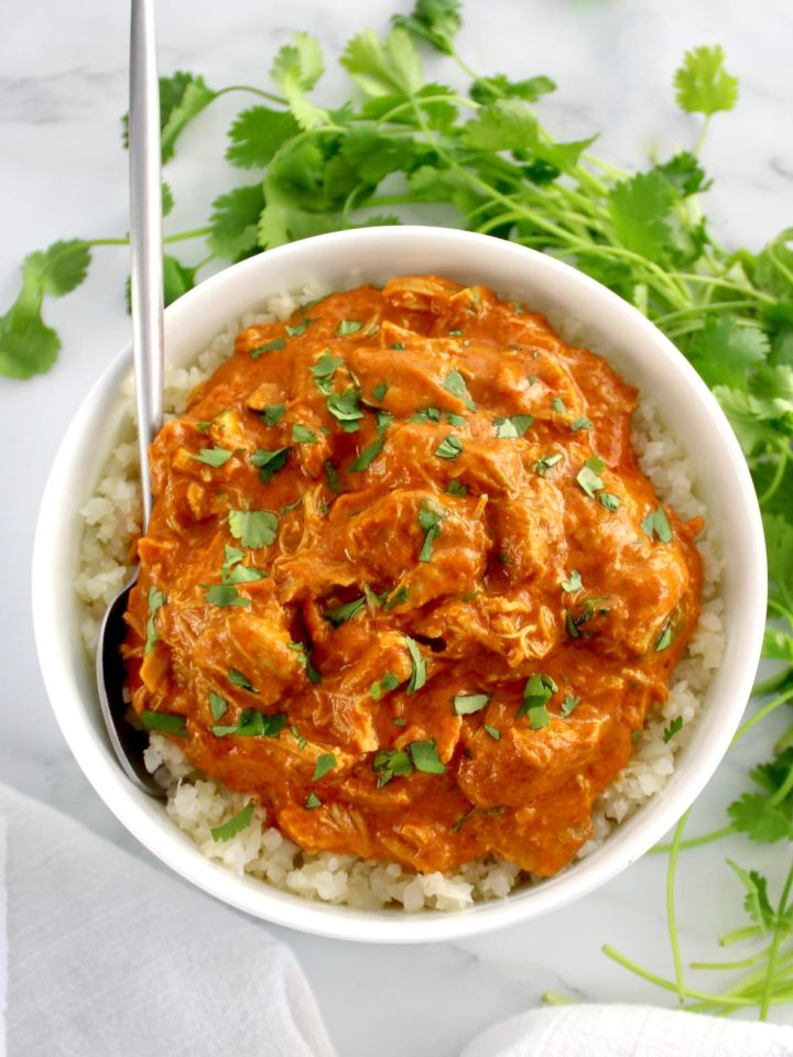 Slow Cooker Butter Chicken in white bowl over cauliflower rice with spoon on side