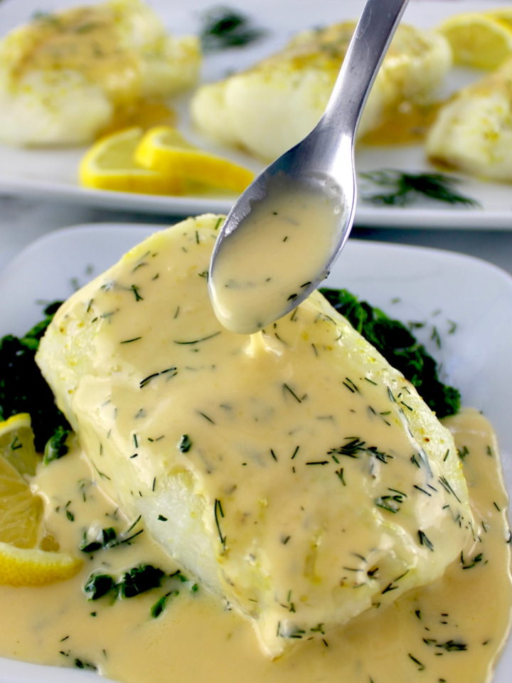 piece of baked cod with lemon beurre blanc being spooned over top