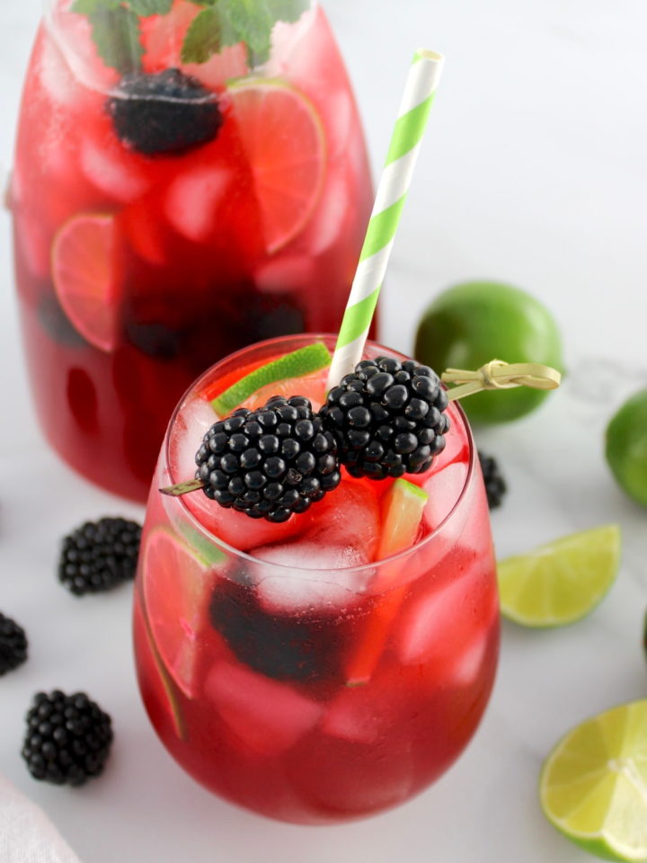 Blackberry Limeade in glass with blackberries garnish and pitcher in back