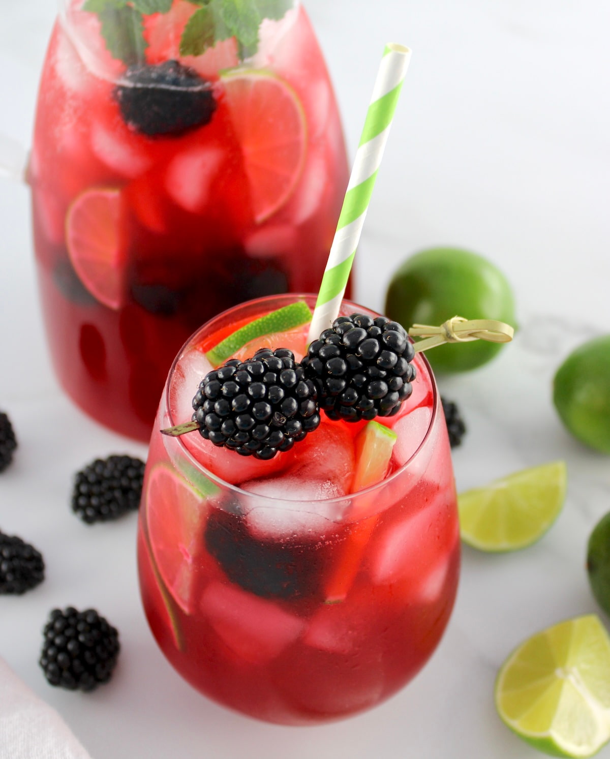 Blackberry Limeade in glass with blackberries garnish and pitcher in back