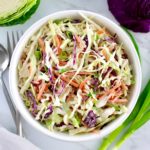 Classic Coleslaw in white bowl with cabbage and scallions in back