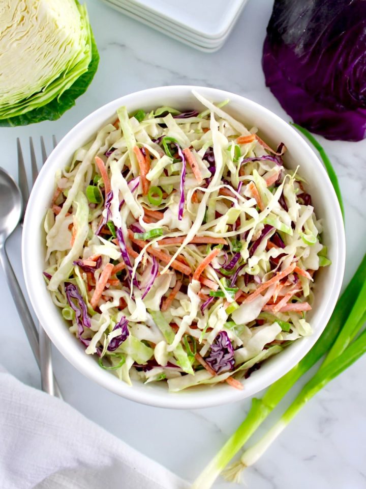 Classic Coleslaw in white bowl with cabbage and scallions in back