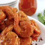 Hot Honey Fried Shrimp piled up on white plate with hot honey in jar in back