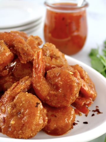 Hot Honey Fried Shrimp piled up on white plate with hot honey in jar in back