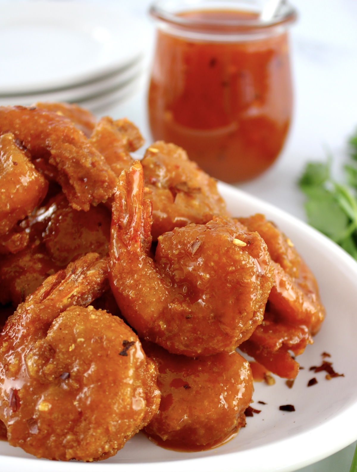Hot Honey Fried Shrimp piled up on white plate with hot honey in jar in back