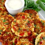 Cheesy Chicken Fritters on white platter with dipping sauce and fresh parsley on side
