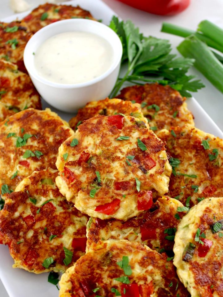 Cheesy Chicken Fritters on white platter with dipping sauce and fresh parsley on side