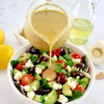 Greek Salad Dressing being poured over salad in white bowl